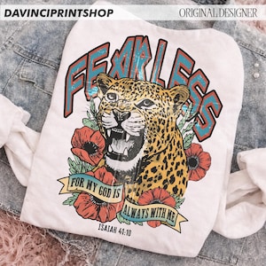 Puede incluir: Camiseta blanca con una ilustraci&oacute;n de leopardo y la palabra "FEARLESS" en verde azulado y rojo. El dise&ntilde;o incluye amapolas rojas y el texto "FOR MY GOD IS ALWAYS WITH ME" e "ISAIAH 41:10".