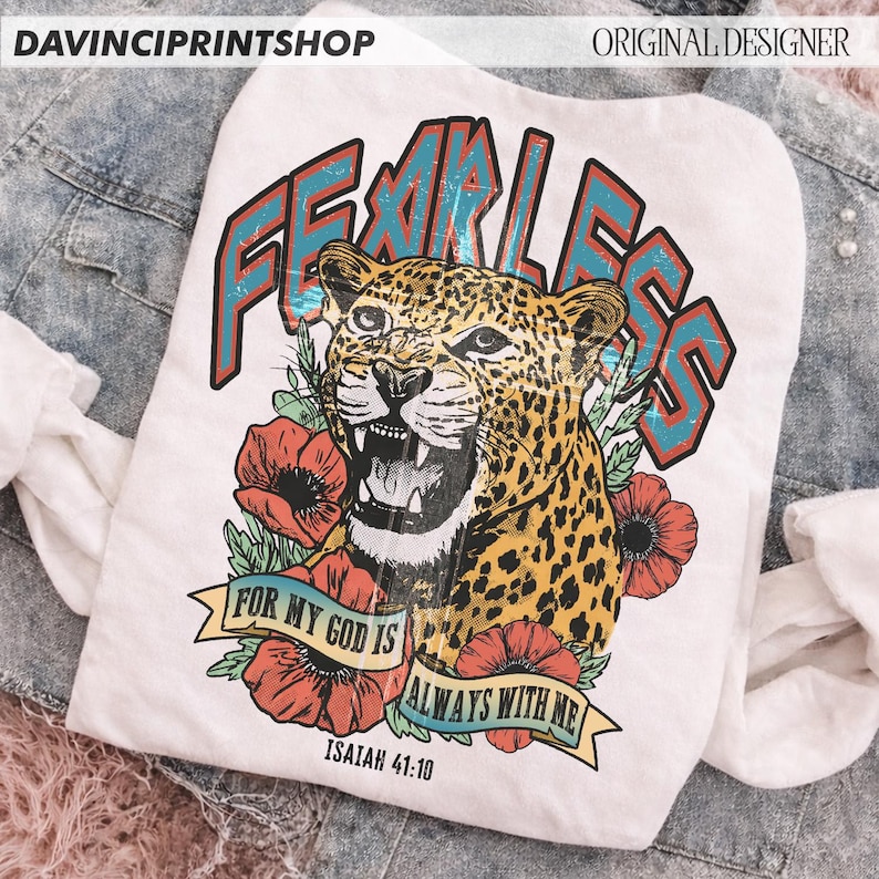 Puede incluir: Camiseta blanca con una ilustraci&oacute;n de leopardo y la palabra "FEARLESS" en verde azulado y rojo. El dise&ntilde;o incluye amapolas rojas y el texto "FOR MY GOD IS ALWAYS WITH ME" e "ISAIAH 41:10".
