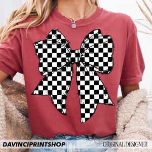 May include: A maroon t-shirt featuring a large bow design with a black and white checkered pattern. The text "DAVINCIPRINTSHOP" is at the bottom left, and "ORIGINAL DESIGNER" is at the bottom right.