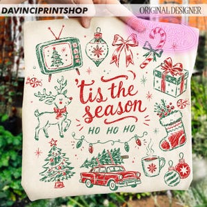 May include: A cream-colored tote bag featuring red and green Christmas illustrations including a vintage television, reindeer, car with a tree, gift, stocking, and ornaments. The text reads 'tis the season' and 'HO HO HO' in red script.