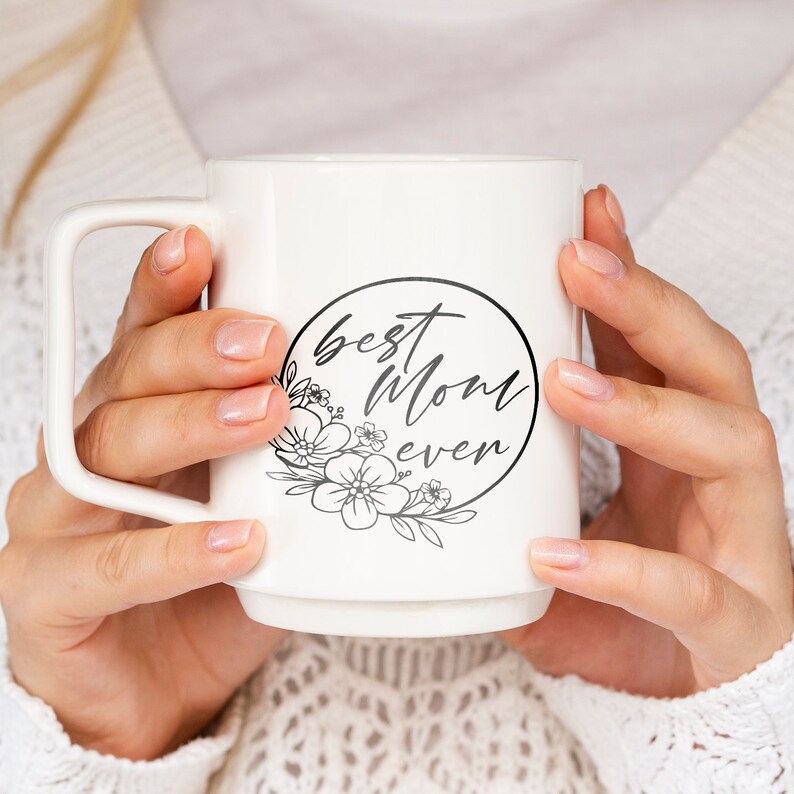 Pode incluir: Caneca de cer&acirc;mica branca com um design circular preto que diz "best mom ever" com um design floral ao redor do c&iacute;rculo.