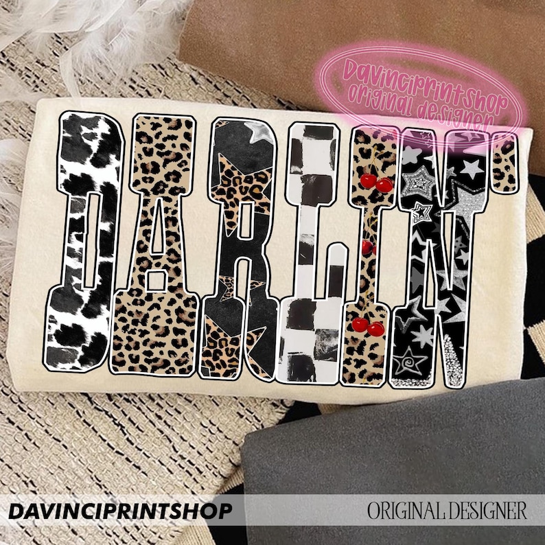 May include: A cream-colored graphic featuring the word "DARLIN" in a bold, stylized font. Each letter is filled with a unique pattern, including cow print, leopard print, stars, and cherries. The text "DAVINCIPRINTSHOP" and "ORIGINAL DESIGNER" are also visible.