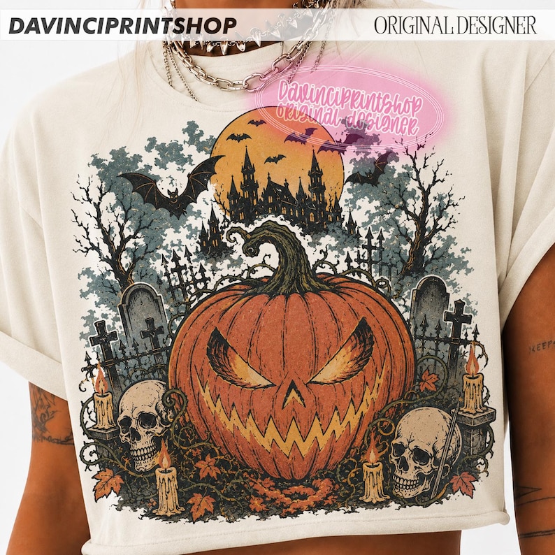 May include: A cream-coloured t-shirt featuring a graphic print of a large orange jack-o'-lantern, two human skulls, lit candles, and a spooky castle silhouette under a full moon with bats. The text DAVINCIPRINTSHOP appears at the top.