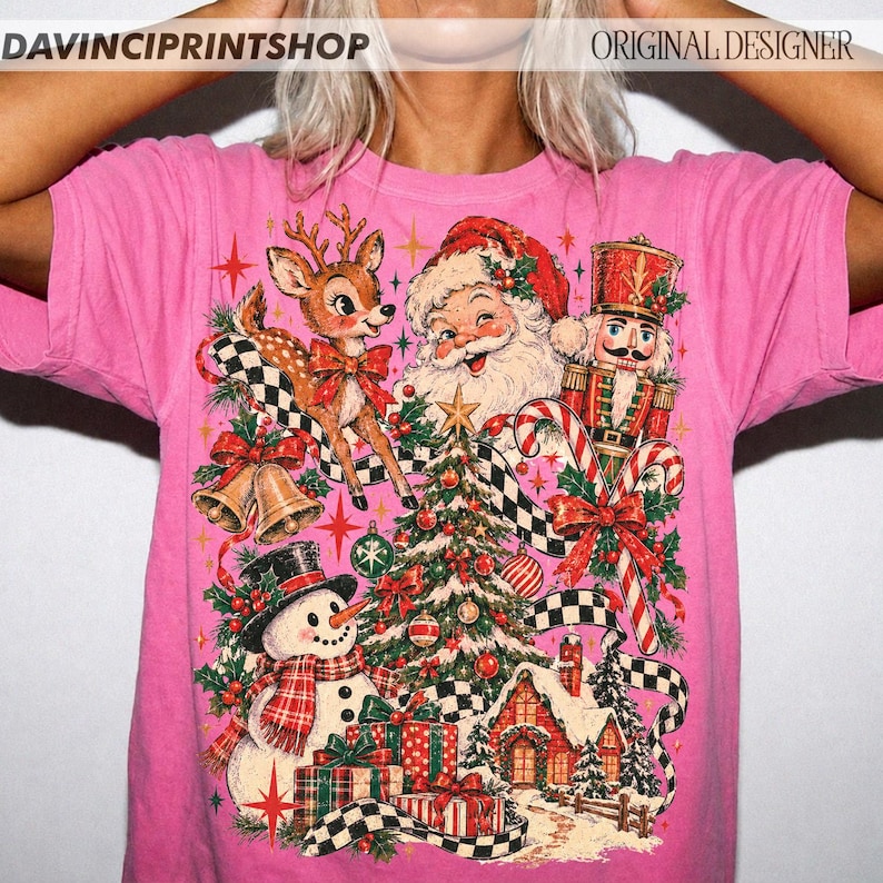 May include: A bright pink t-shirt featuring a festive Christmas graphic with a reindeer, Santa Claus, a nutcracker, a snowman, a decorated tree, wrapped gifts, bells, and a small house. The text DAVINCIPRINTSHOP and ORIGINAL DESIGNER appears at the top.