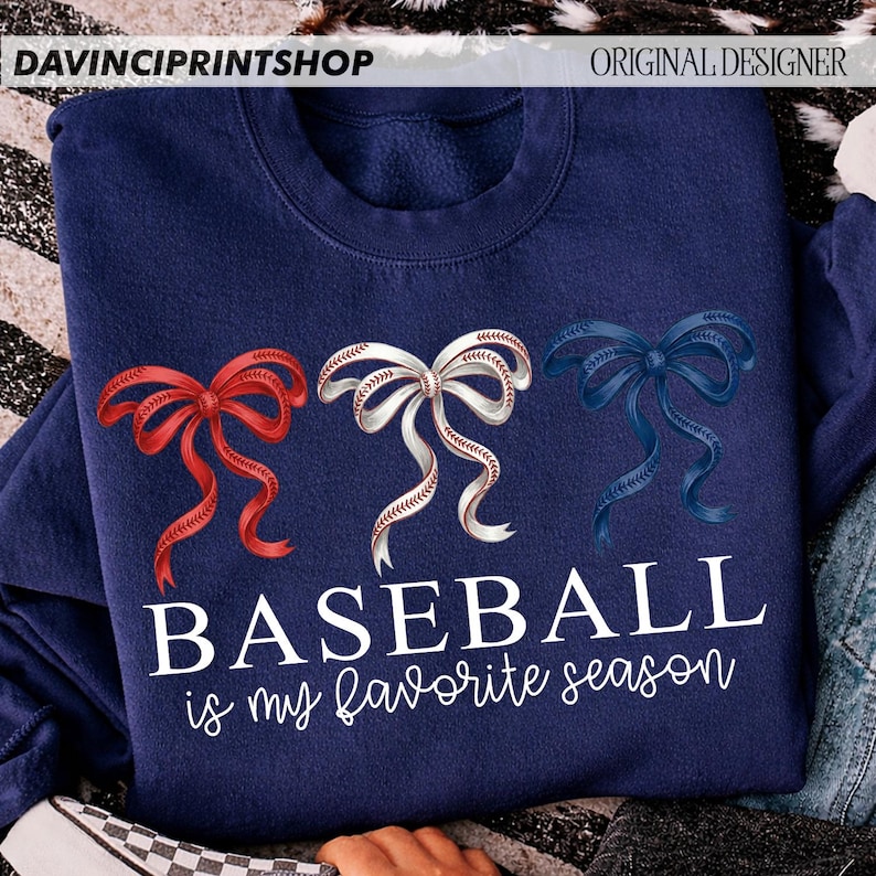 May include: Navy blue sweatshirt with three decorative bows in red, white, and blue. The white bow is designed to look like a baseball. The text "BASEBALL is my favorite season" is printed in white script.