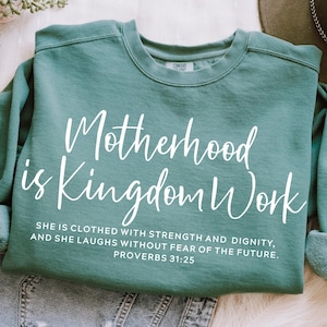 May include: Teal blue sweatshirt with white text that reads "Motherhood is Kingdom Work" and a quote from Proverbs 31:25.  The quote reads "She is clothed with strength and dignity, and she laughs without fear of the future."