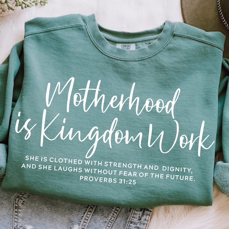 May include: Teal blue sweatshirt with white text that reads "Motherhood is Kingdom Work" and a quote from Proverbs 31:25.  The quote reads "She is clothed with strength and dignity, and she laughs without fear of the future."
