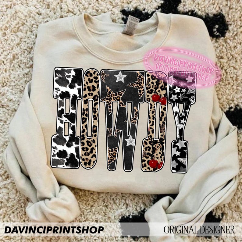 May include: A beige sweatshirt with the word "COWBOY" in a bold, block letter design. The letters feature a mix of patterns, including cow print, leopard print, stars, and cherries. The text "DAVINCIPRINTSHOP" and "ORIGINAL DESIGNER" are also visible.