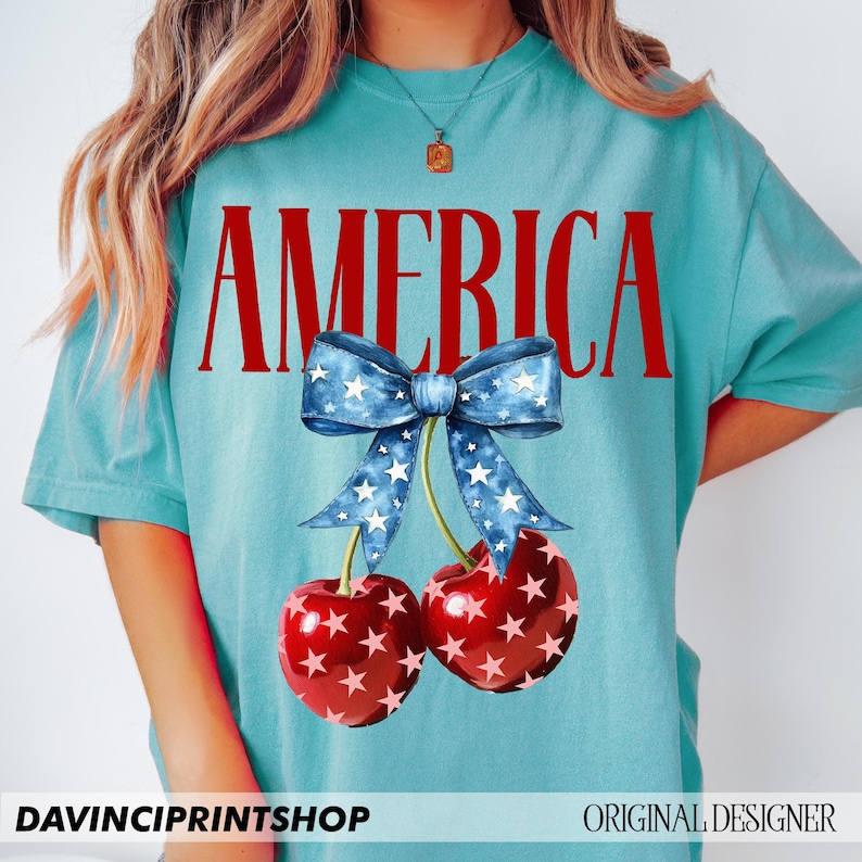 May include: A turquoise blue t-shirt with the word "AMERICA" printed in red letters. A blue and white bow with white stars is above two red cherries with white stars.