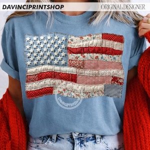 May include: A light blue t-shirt featuring a patchwork American flag design. The flag incorporates white stars on a blue field and red and white stripes with floral and gingham patterns. The text "DAVINCIPRINTSHOP" is visible at the top.