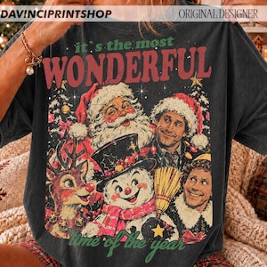 K&ouml;nnte beinhalten: Ein anthrazitfarbenes T-Shirt mit einem Grafikdruck und dem Text 'it's the most WONDERFUL time of the year'. Das Design zeigt Illustrationen vom Weihnachtsmann, einem Rentier, einem Schneemann und einem Mann mit Weihnachtsm&uuml;tze.