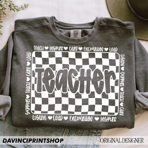 May include: Gray sweatshirt with a white checkered design and the word "Teacher" in a white bubble font. The words "Listen, Support, Teach, Care, Inspire, Encourage, Lead" are written around the checkered design.