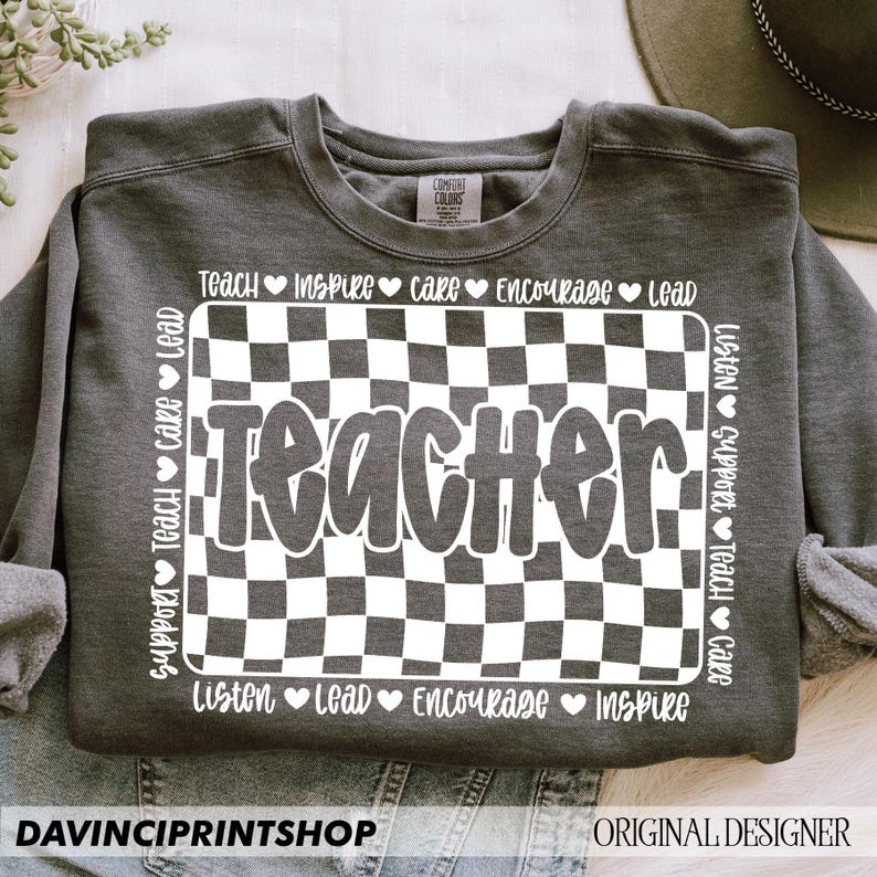May include: Gray sweatshirt with a white checkered design and the word "Teacher" in a white bubble font. The words "Listen, Support, Teach, Care, Inspire, Encourage, Lead" are written around the checkered design.