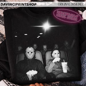 Peut inclure: Un sweat-shirt noir &agrave; col rond avec une impression graphique de personnages de films d'horreur assis dans une salle de cin&eacute;ma. L'image montre Jason Voorhees avec un seau de pop-corn et Michael Myers tenant une boisson, avec d'autres silhouettes.