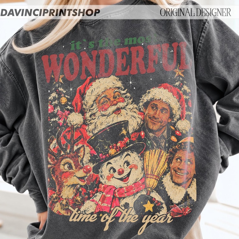 K&ouml;nnte beinhalten: Ein anthrazitfarbenes Sweatshirt mit Rundhalsausschnitt und einem Grafikdruck mit dem Text 'it's the most WONDERFUL time of the year'. Das Design zeigt Illustrationen vom Weihnachtsmann, einem Schneemann, einem Rentier und zwei Personen.