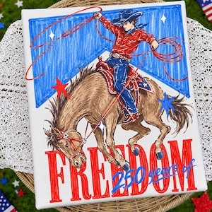 May include: A canvas print featuring a cowboy riding a bucking bronco, roping with a red lasso. The artwork is in red, blue, and brown, with the word "FREEDOM" and "250 years of" in red text. Stars and a blue banner are in the background.