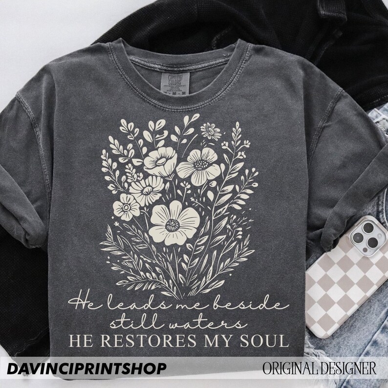 May include: A gray t-shirt with a floral design and the text "He leads me beside still waters HE RESTORES MY SOUL".