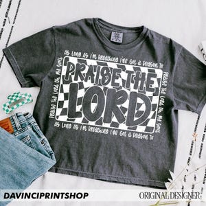 May include: A dark gray t-shirt with a white checkered pattern and the text "Praise the Lord Oh, My Soul" and "As Long As I'm Breathing I've Got a Reason To" printed on it.