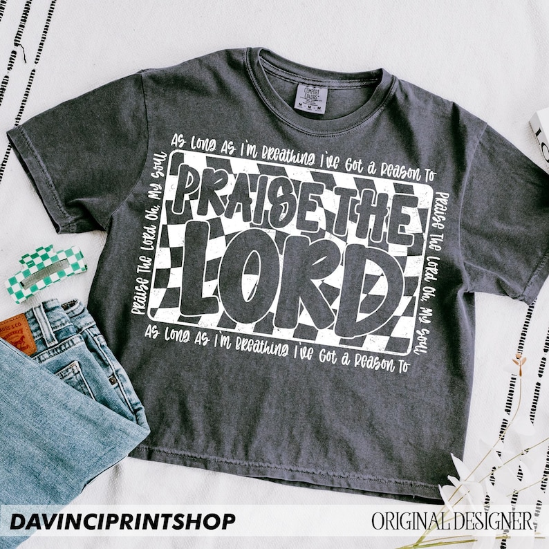 May include: A dark gray t-shirt with a white checkered pattern and the text "Praise the Lord Oh, My Soul" and "As Long As I'm Breathing I've Got a Reason To" printed on it.