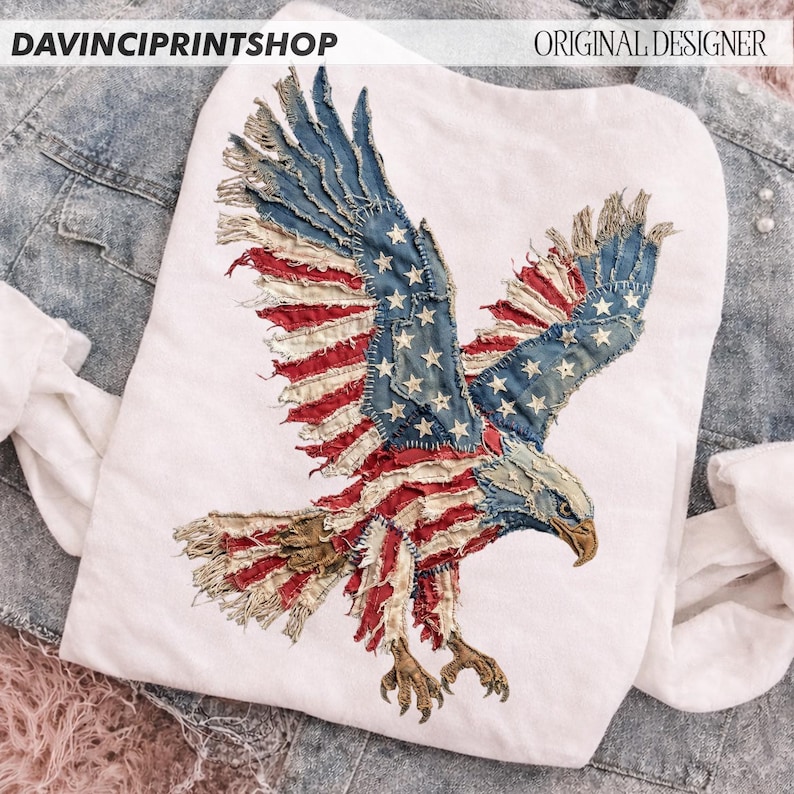 Pu&ograve; includere: T-shirt bianca con un design di aquila della bandiera americana invecchiata. Le ali dell'aquila sono spiegate, mostrando le strisce rosse e bianche e le stelle blu. I testi "DAVINCIPRINTSHOP" e "ORIGINAL DESIGNER" sono visibili.