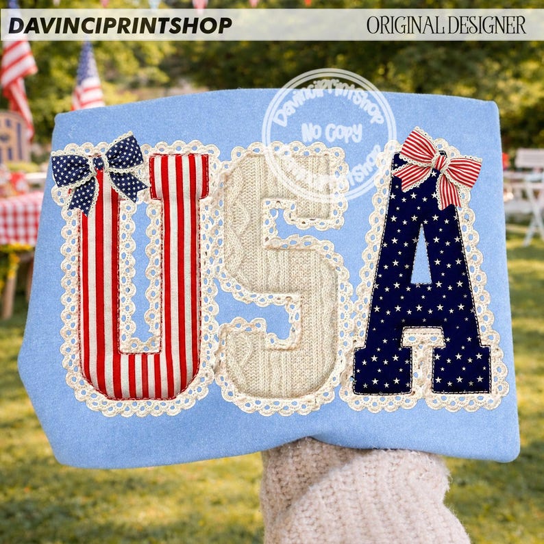May include: A light blue decorative item with the letters "USA" in red, white, and blue. The "U" has red and white stripes, the "S" is a cable knit design, and the "A" is navy blue with white stars. Each letter is outlined with white lace and topped with a bow.