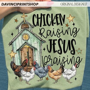 Peut inclure: T-shirt vert clair avec une illustration d'une petite &eacute;glise avec une croix, des &eacute;toiles et des poulets. Le texte se lit comme suit : "Chicken Raising Jesus Praising."