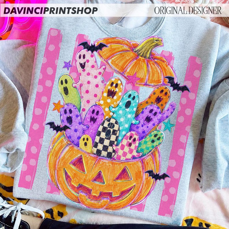 May include: A light gray sweatshirt featuring a graphic of two orange pumpkins filled with colorful, patterned ghosts and small black bats. The design includes pink vertical stripes with white polka dots and the text DAVINCIPRINTSHOP.
