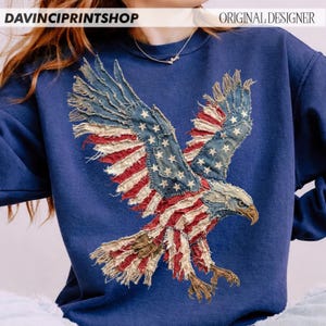 Pu&ograve; includere: Una felpa blu navy con un design di aquila della bandiera americana invecchiata. Le ali dell'aquila sono fatte di strisce rosse e bianche e toppe blu con stelle bianche. I testi "DAVINCIPRINTSHOP" e "ORIGINAL DESIGNER" sono visibili.