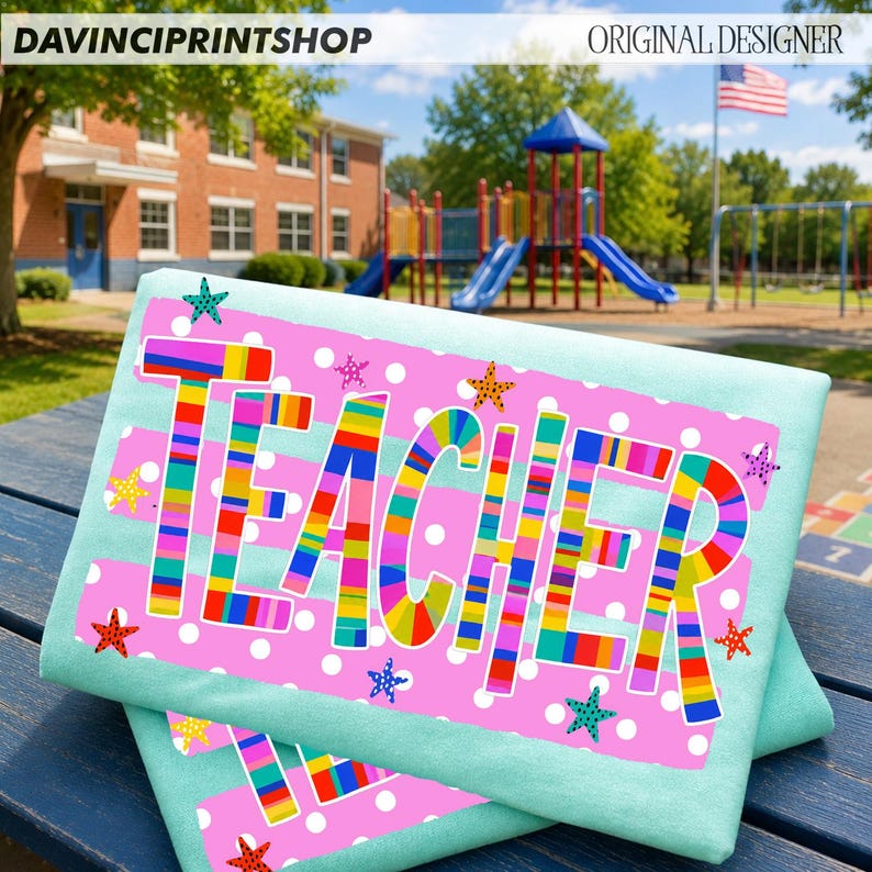 May include: A light blue t-shirt featuring a pink rectangular graphic with white polka dots and the word TEACHER in large, multi-colored striped letters. The design includes small, colorful starfish scattered across the pink background.