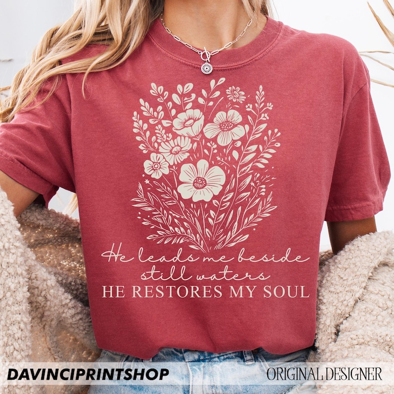 May include: A red t-shirt with a white floral design and the text "He leads me beside still waters HE RESTORES MY SOUL".