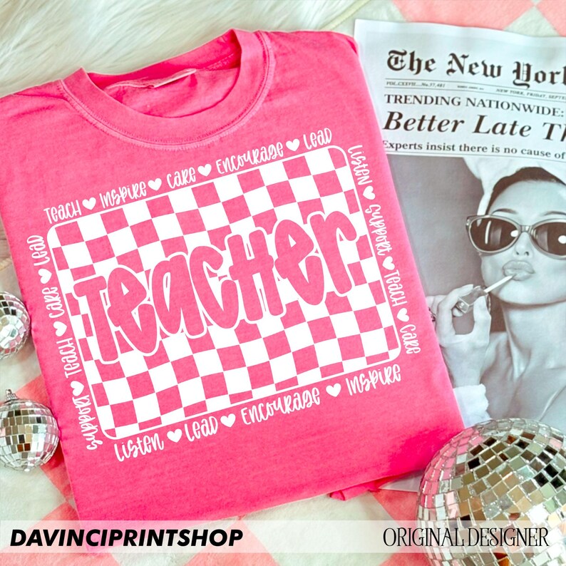 May include: Pink t-shirt with a white checkered design and the word "Teacher" in white letters. The checkered design is surrounded by a white border with the words "Teach", "Inspire", "Care", "Encourage", "Lead", "Listen", "Support", "Teach", "Care", "Listen", "Lead", "Encourage", "Inspire" written around the border.