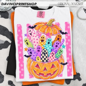 May include: A white t-shirt featuring a graphic of a large orange jack-o'-lantern filled with colorful ghosts in various patterns like polka dots and checkers. Small black bats and stars surround the pumpkin, which sits atop a pink striped background.