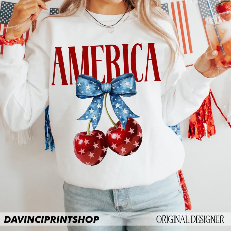 May include: White sweatshirt with the word "AMERICA" in red letters and a blue and white bow with stars above two red cherries with white stars.