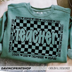 May include: Teal blue sweatshirt with a black and white checkered design and the word "Teacher" in a teal blue font. The words "Teach, Inspire, Care, Encourage, Lead, Listen, Support, Teach, Care" are written around the checkered design.
