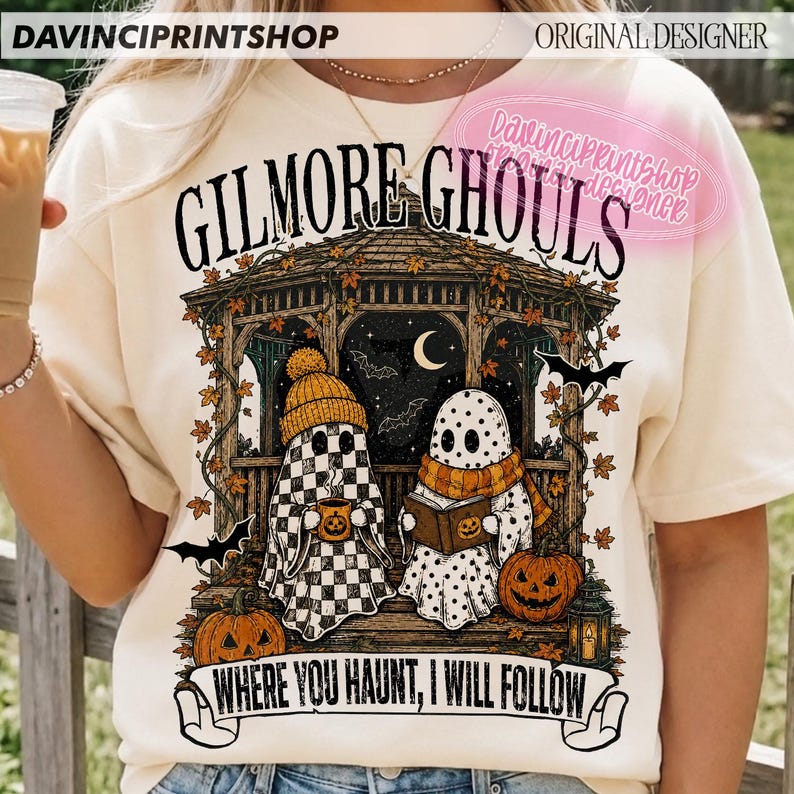Puede incluir: Una camiseta color crema con un gr&aacute;fico de dos fantasmas en un cenador con el texto "GILMORE GHOULS" y "WHERE YOU HAUNT, I WILL FOLLOW". El dise&ntilde;o incluye calabazas, hojas de oto&ntilde;o, murci&eacute;lagos, una luna creciente y un farol.