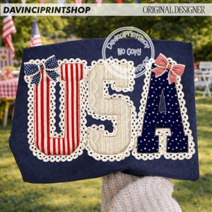 May include: Navy blue fabric with the letters "USA" appliqued in red and white stripes, cream cable knit, and navy blue with white stars. Each letter is outlined with white lace and topped with a bow. The text "DAVINCIPRINTSHOP" and "ORIGINAL DESIGNER" are visible.
