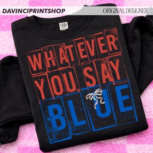以下が含まれることがあります： 赤と青のブロック文字で「WHATEVER YOU SAY BLUE」と書かれた黒いスウェットシャツ。シルバーのリボンピンが「BLUE」の文字に付いています。スウェットシャツはクルーネックと長袖です。