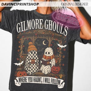 Puede incluir: Una camiseta gris carb&oacute;n con un estampado gr&aacute;fico que incluye el texto "GILMORE GHOULS" y "WHERE YOU HAUNT, I WILL FOLLOW". El dise&ntilde;o muestra dos fantasmas en un cenador con hojas de oto&ntilde;o, calabazas, murci&eacute;lagos y una luna creciente.