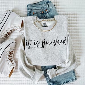 May include: Gray sweatshirt with the text "it is finished" and the scripture reference "JOHN 10:28-30" in black lettering.