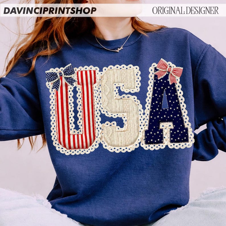 May include: Navy blue sweatshirt with the word "USA" appliqued on the front. The letters are decorated with red and white stripes, a cable knit pattern, and a navy blue star pattern. Each letter is outlined with white lace and topped with a bow.