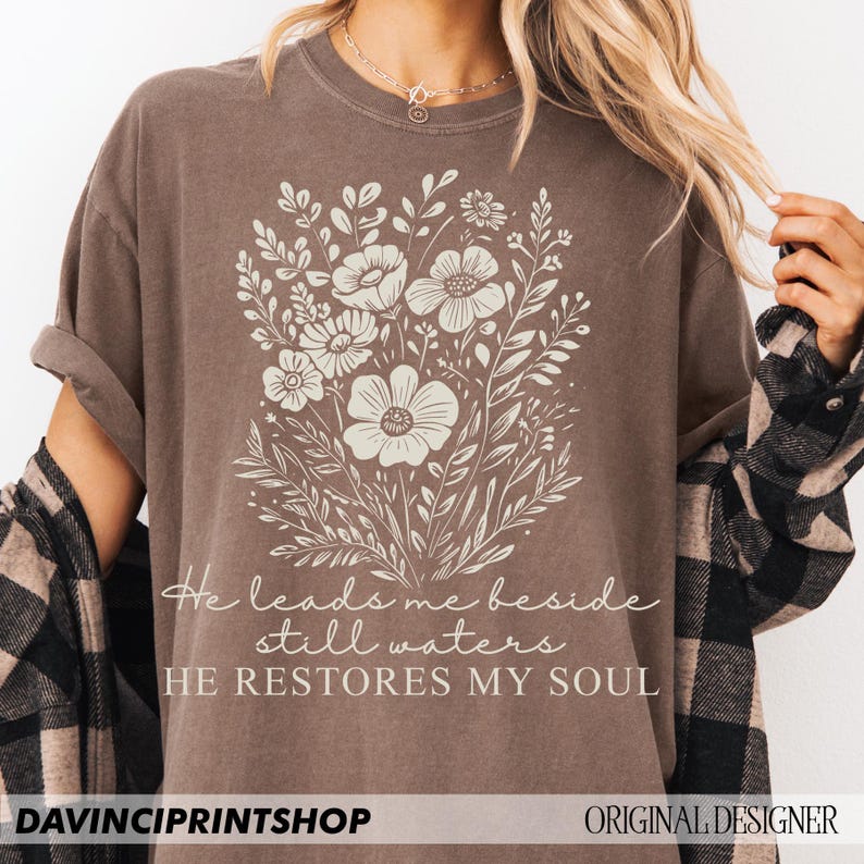 May include: A brown t-shirt with a floral design and the text "He leads me beside still waters HE RESTORES MY SOUL".