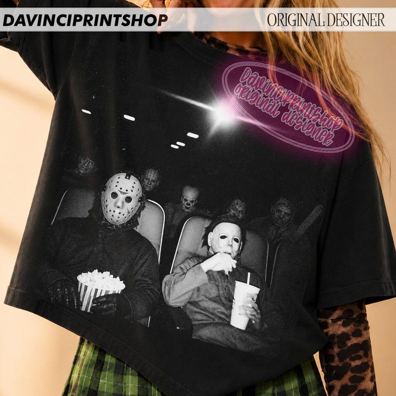 Peut inclure: Un t-shirt noir &agrave; manches courtes avec une impression graphique de personnages de films d'horreur assis dans une salle de cin&eacute;ma. L'image montre des personnages masqu&eacute;s, dont un masque de hockey, tenant du pop-corn. Texte DAVINCIPRINTSHOP.