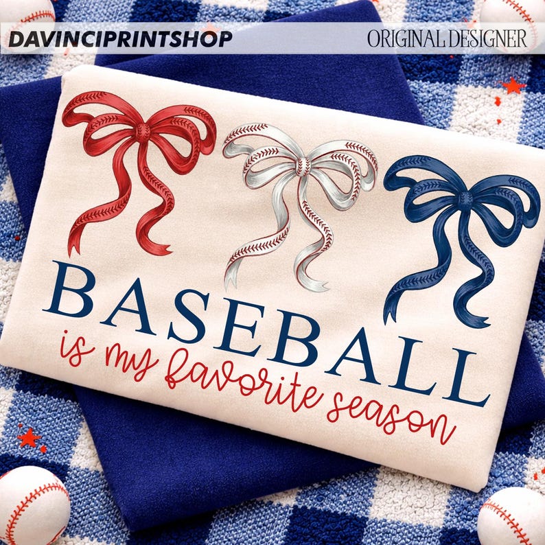 May include: A cream-colored t-shirt with three decorative bows in red, white, and blue. The white bow has baseball stitching. The text "BASEBALL is my favorite season" is printed in navy and red.