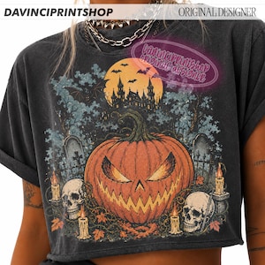 May include: A charcoal grey t-shirt featuring a graphic print of a large orange jack-o'-lantern with a menacing expression, surrounded by skulls, lit candles, a haunted castle silhouette, a full moon, and bats against a dark, spooky background.