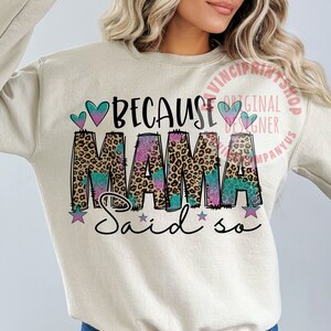 May include: A beige sweatshirt with the text "Because Mama Said So" in black, pink, and blue. The word "Mama" is in a leopard print with a glittery effect. There are two pink hearts and two blue hearts above the text. There are three stars below the text.