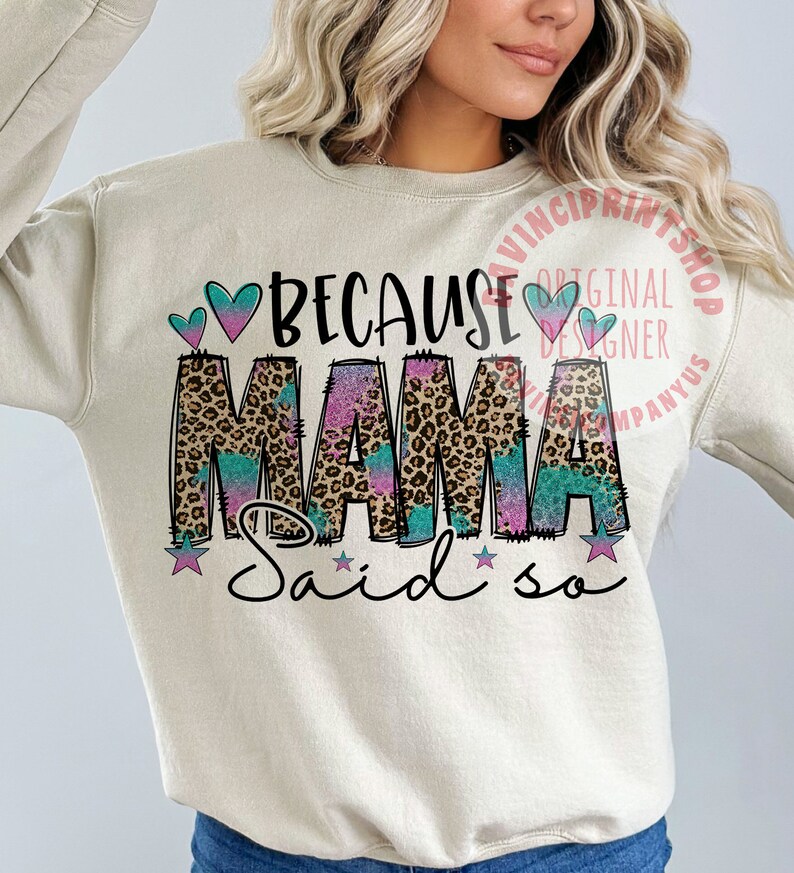 May include: A beige sweatshirt with the text "Because Mama Said So" in black, pink, and blue. The word "Mama" is in a leopard print with a glittery effect. There are two pink hearts and two blue hearts above the text. There are three stars below the text.