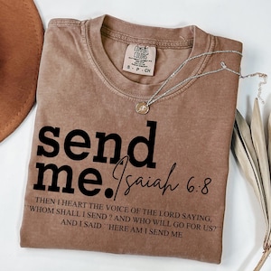 Pode incluir: Uma camiseta marrom com o texto "send me. Isaiah 6.8" e uma cita&ccedil;&atilde;o da B&iacute;blia: "Ent&atilde;o ouvi a voz do Senhor que dizia: Quem enviarei? E quem ir&aacute; por n&oacute;s?" E eu disse: "Eis-me aqui, envia-me."