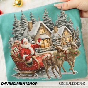 May include: A teal sweatshirt with a festive Christmas design. It depicts Santa Claus in a red sleigh, pulled by reindeer, with snow-covered houses and pine trees in the background. The text "DAVINCIPRINTSHOP" and "ORIGINAL DESIGNER" are visible.