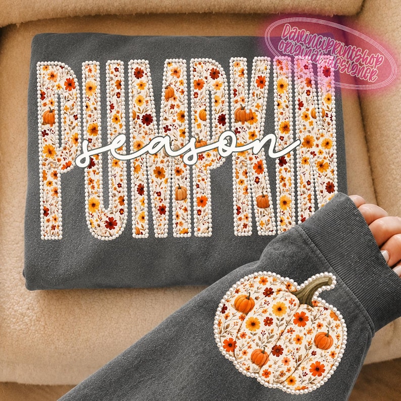 May include: A dark gray sweatshirt featuring the word PUMPKIN in large block letters filled with a floral and pumpkin pattern, outlined in white dots. The word season is written in white cursive script. A pumpkin graphic is on the sleeve.