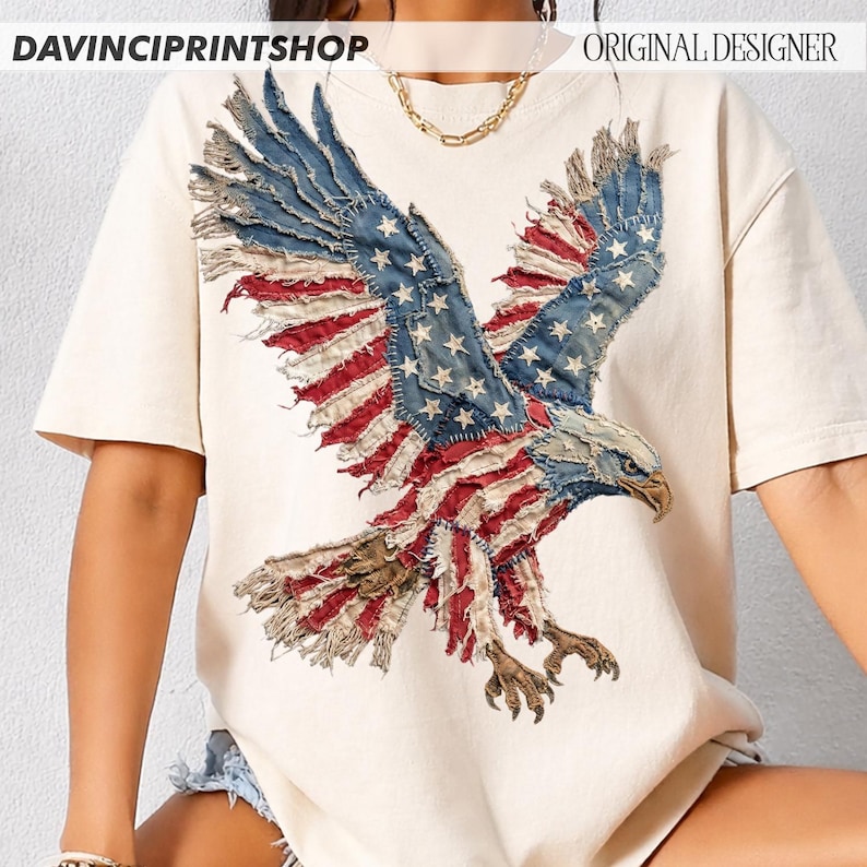 Pu&ograve; includere: T-shirt color crema con un design dettagliato di un'aquila. Le ali dell'aquila sono realizzate con toppe di denim blu con stelle bianche e strisce rosse e bianche, che ricordano la bandiera americana. Il testo "DAVINCIPRINTSHOP" e "ORIGINAL DESIGNER" sono visibili.